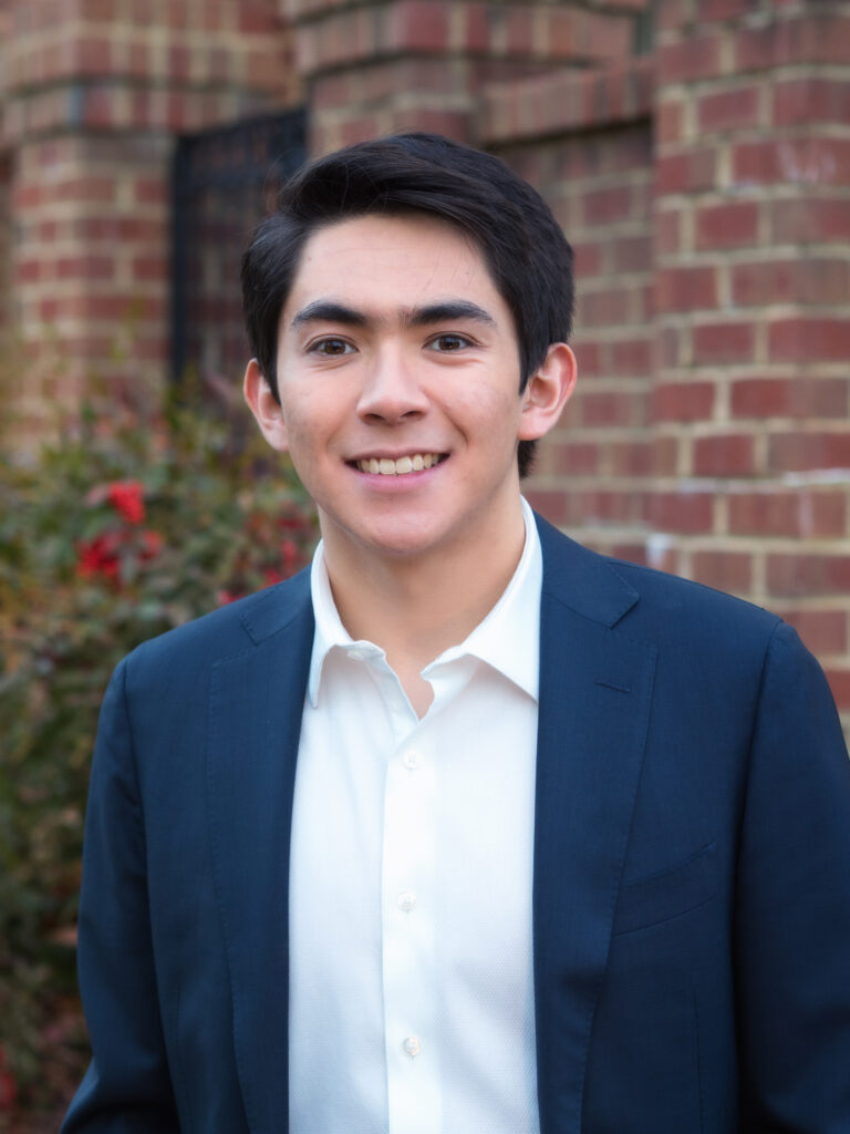Jae wears a navy blue blazer and white shirt in this headshot.